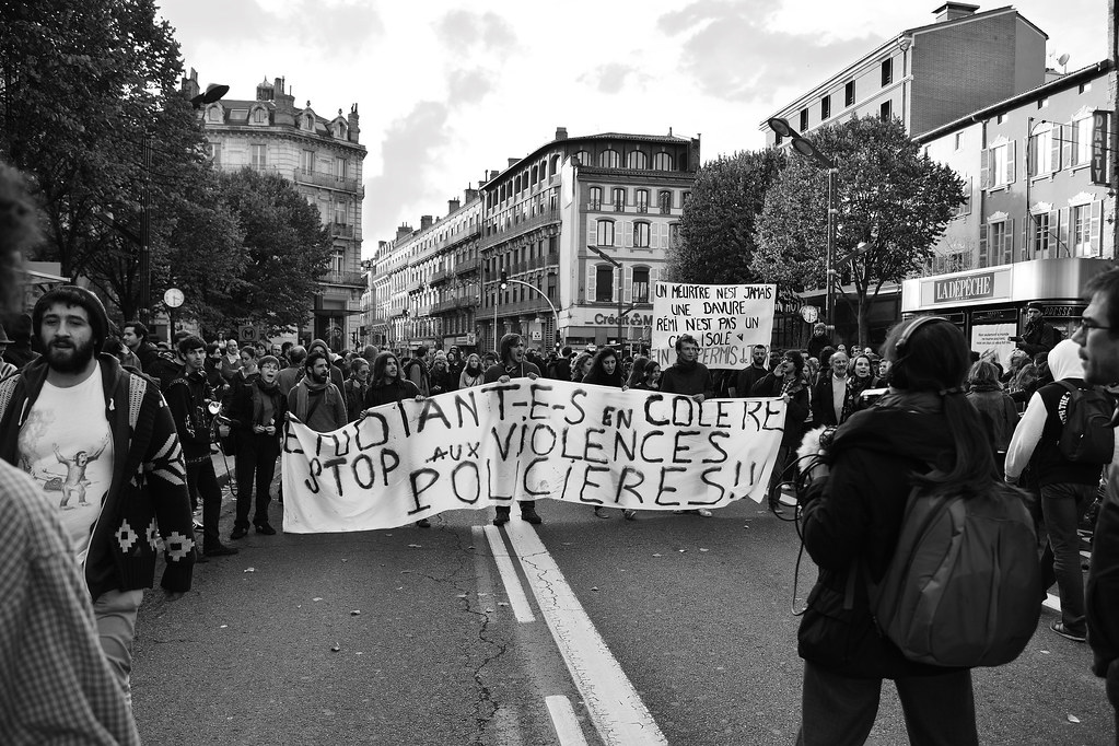 Manifestation en ville avec des personnes défilant derrière une grande banderole dénonçant les violences policières.