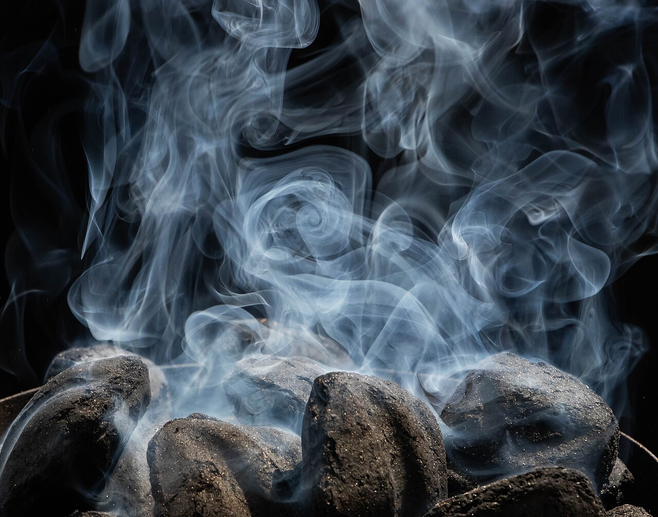 White smoke rising from charcoal briquettes as they start to catch fire and burn.